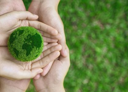 Hands holding a small green globe made of grass, symbolizing environmental sustainability