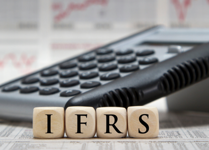 Calculator resting on financial documents with wooden blocks spelling ‘IFRS’ in front