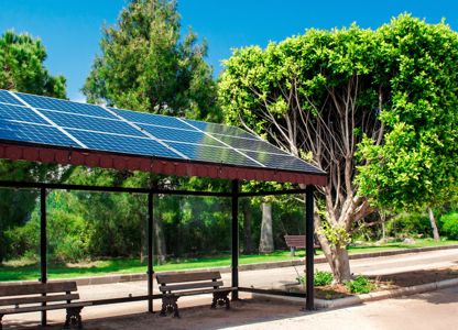 Bus stop shelter fitted with rooftop solar panels, surrounded by trees and greenery on a sunny day