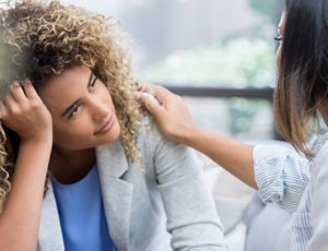 Person comforting someone who is distressed, with a hand placed supportively on their shoulder