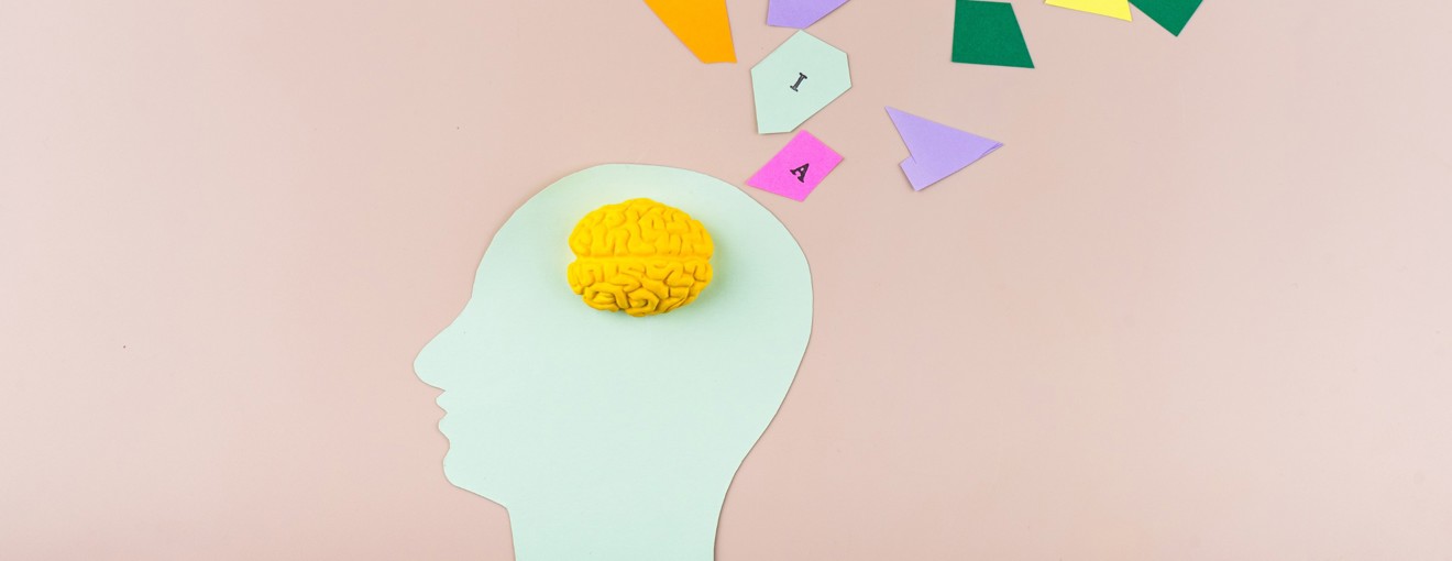 illustration of a human head silhouette with a yellow brain model inside and colourful geometric shapes emerging from it