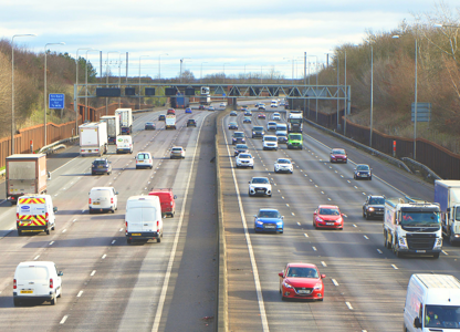 Busy multi‑lane motorway with cars, vans, and lorries travelling in both directions on a clear day