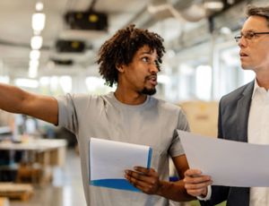 Two people reviewing documents and discussing work inside an industrial or manufacturing facility