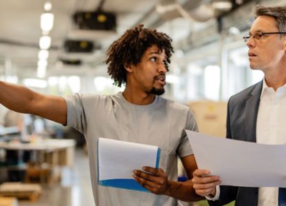 Two people reviewing documents and discussing work inside an industrial or manufacturing facility