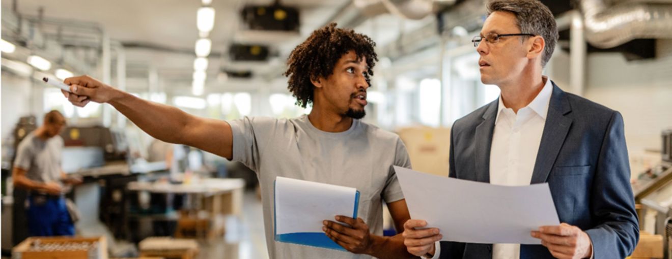 Two people reviewing documents and discussing work inside an industrial or manufacturing facility