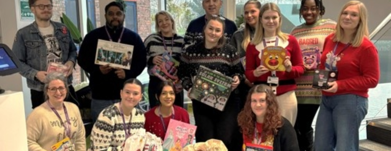 Procurement services team in festive jumpers holding christmas donations 