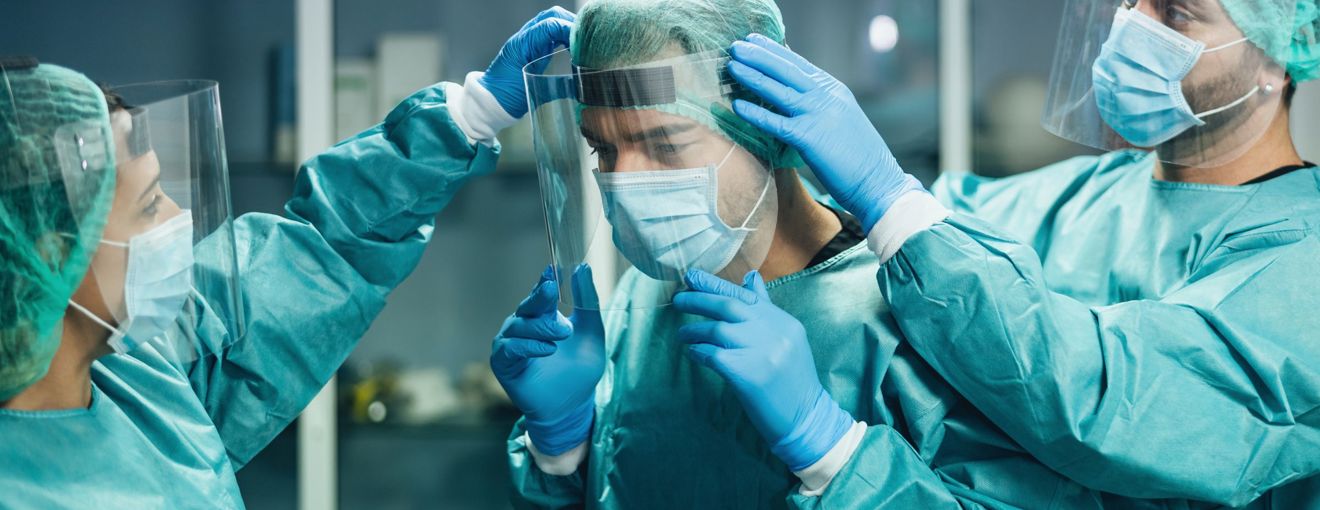 Medical staff wearing protective gowns, gloves, and face shields helping a colleague adjust their protective equipment