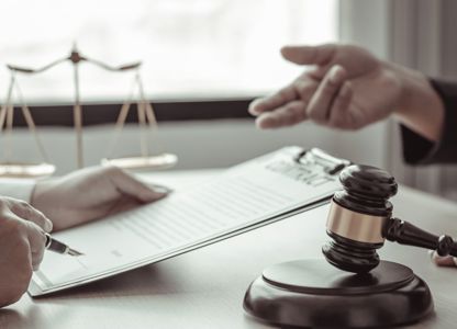 Lawyer reviewing and signing documents on a clipboard as another person gestures during a legal consultation