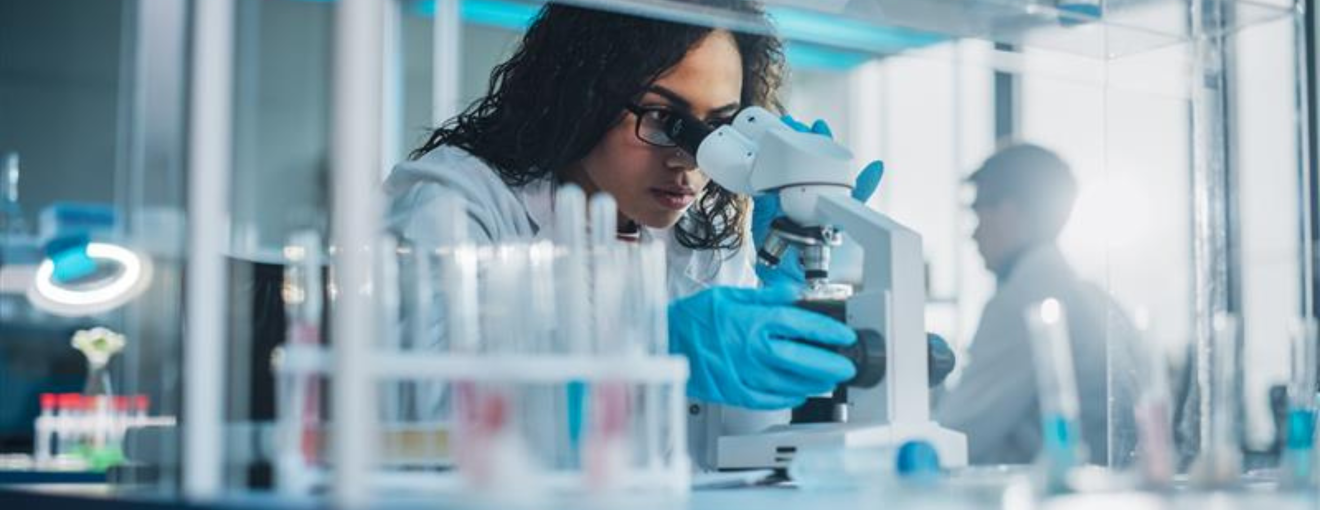 Scientist wearing gloves using a microscope in a laboratory with test tubes and equipment in the foreground